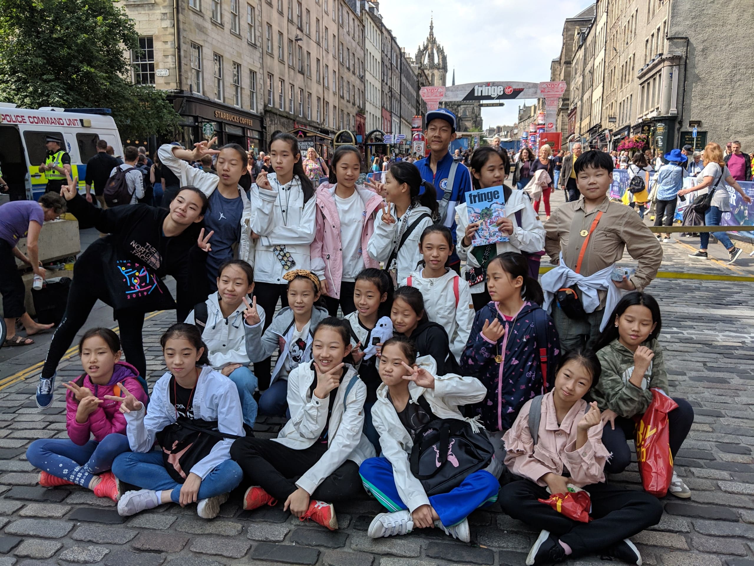 Young dancers from Here Dance sitting together on the cobbles of the Royal Mile in Edinburgh during the 2019 Fringe