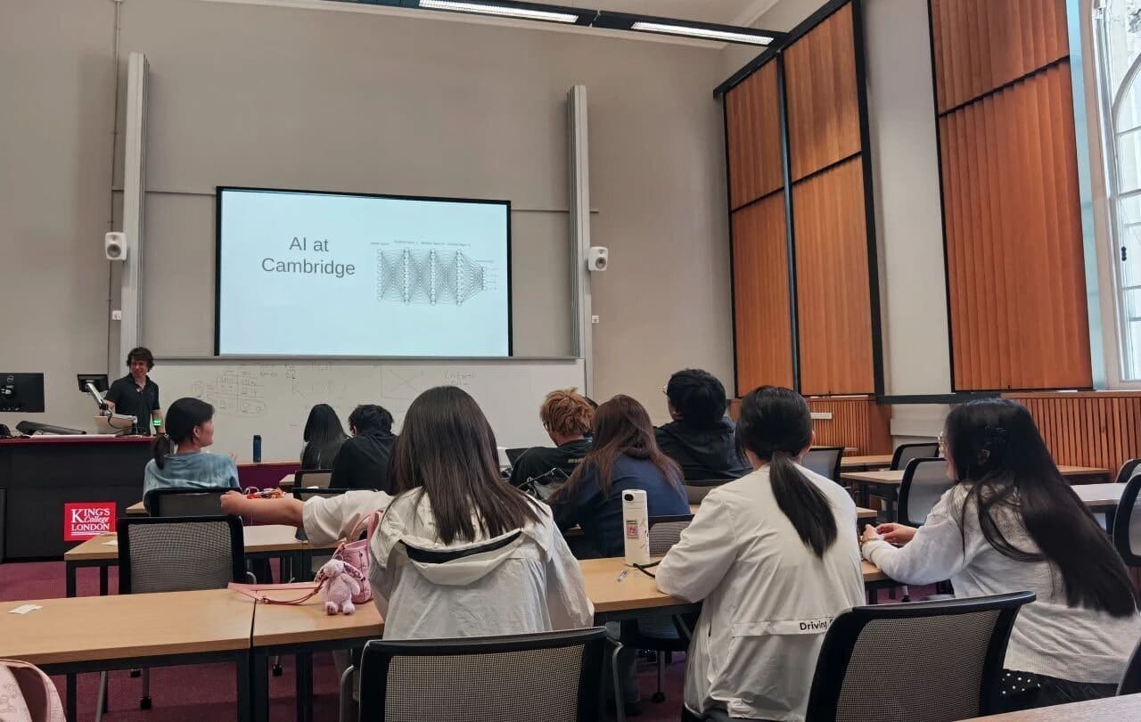 Students in a lecture room at King's College London watching a presentation titled "AI at Cambridge"
