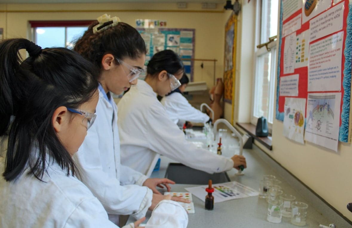 Students in white lab coats and safety glasses carrying out an experiment in a school science lab