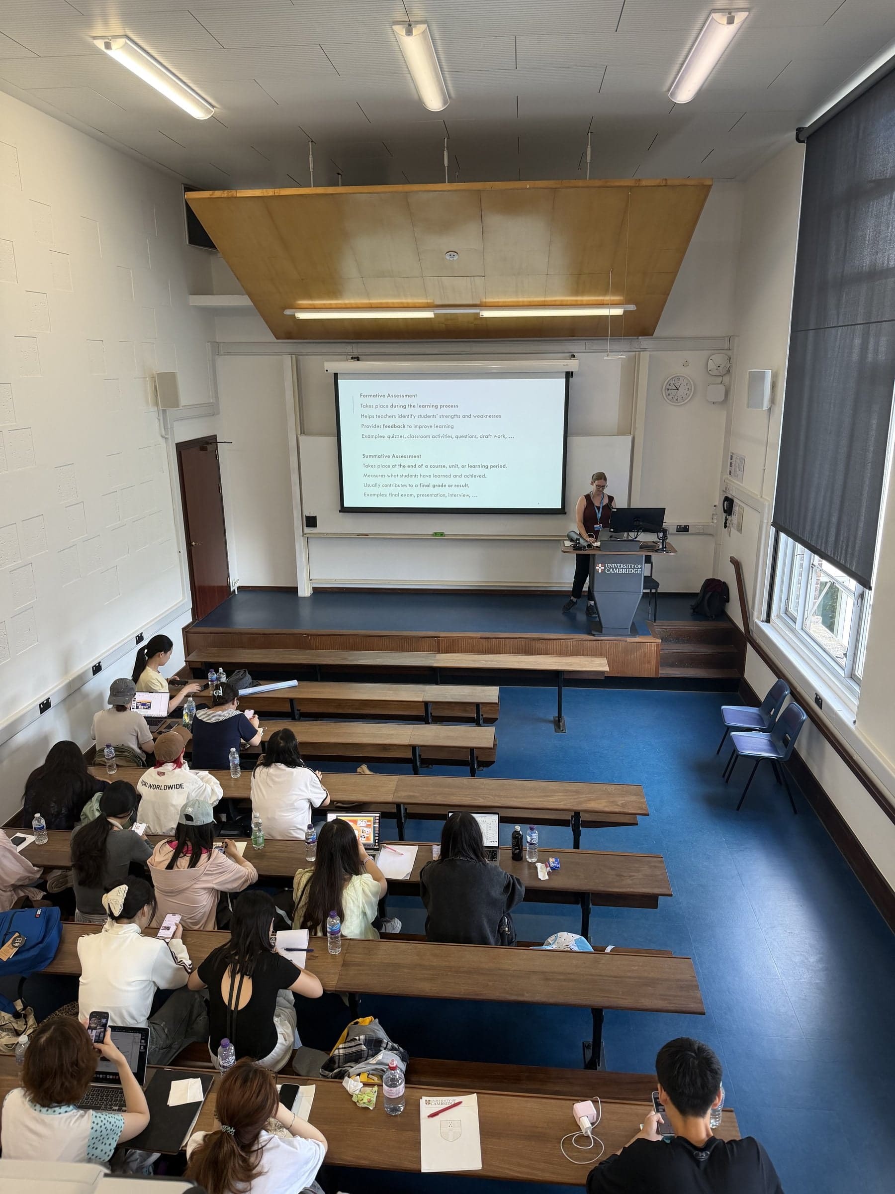 A lecture theatre in Cambridge seen from the back, with a speaker at the front and participants taking notes