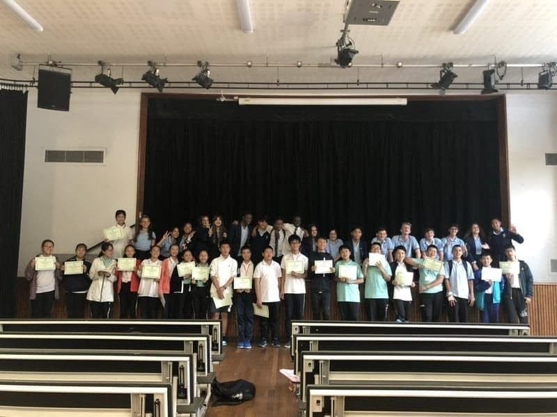 Visiting students holding up their certificates on the stage of a school hall