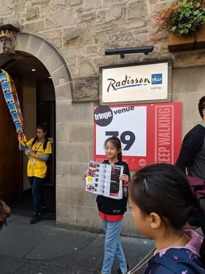 A student holding up a flyer outside Fringe Venue 39 on the Royal Mile