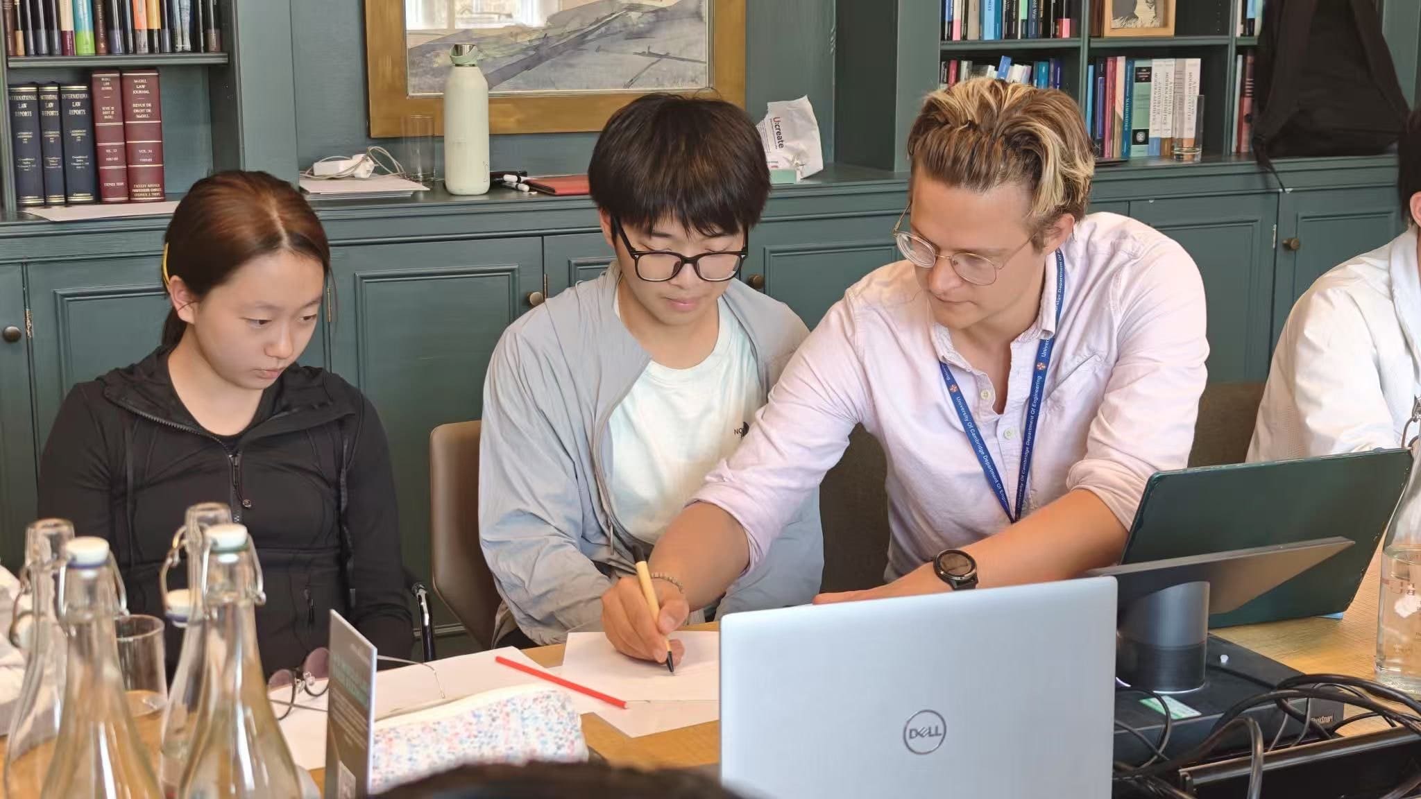 A tutor sitting beside two students, working through a problem on paper