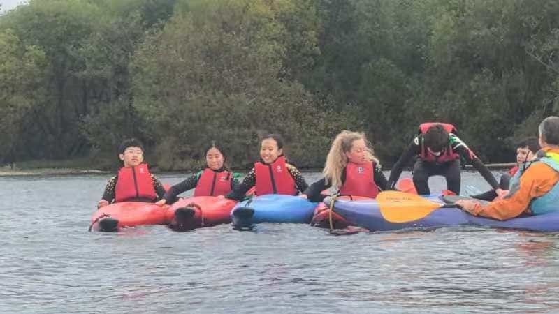 Students and an instructor in kayaks, holding on to each other on the lake