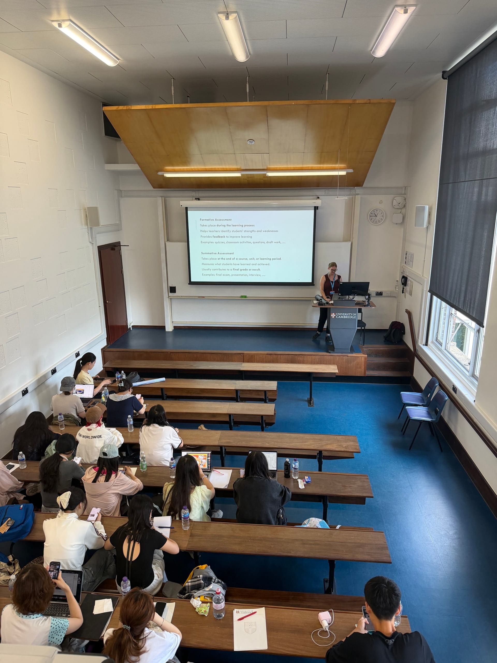 A lecture theatre in Cambridge seen from the back, with a speaker at the front and participants taking notes